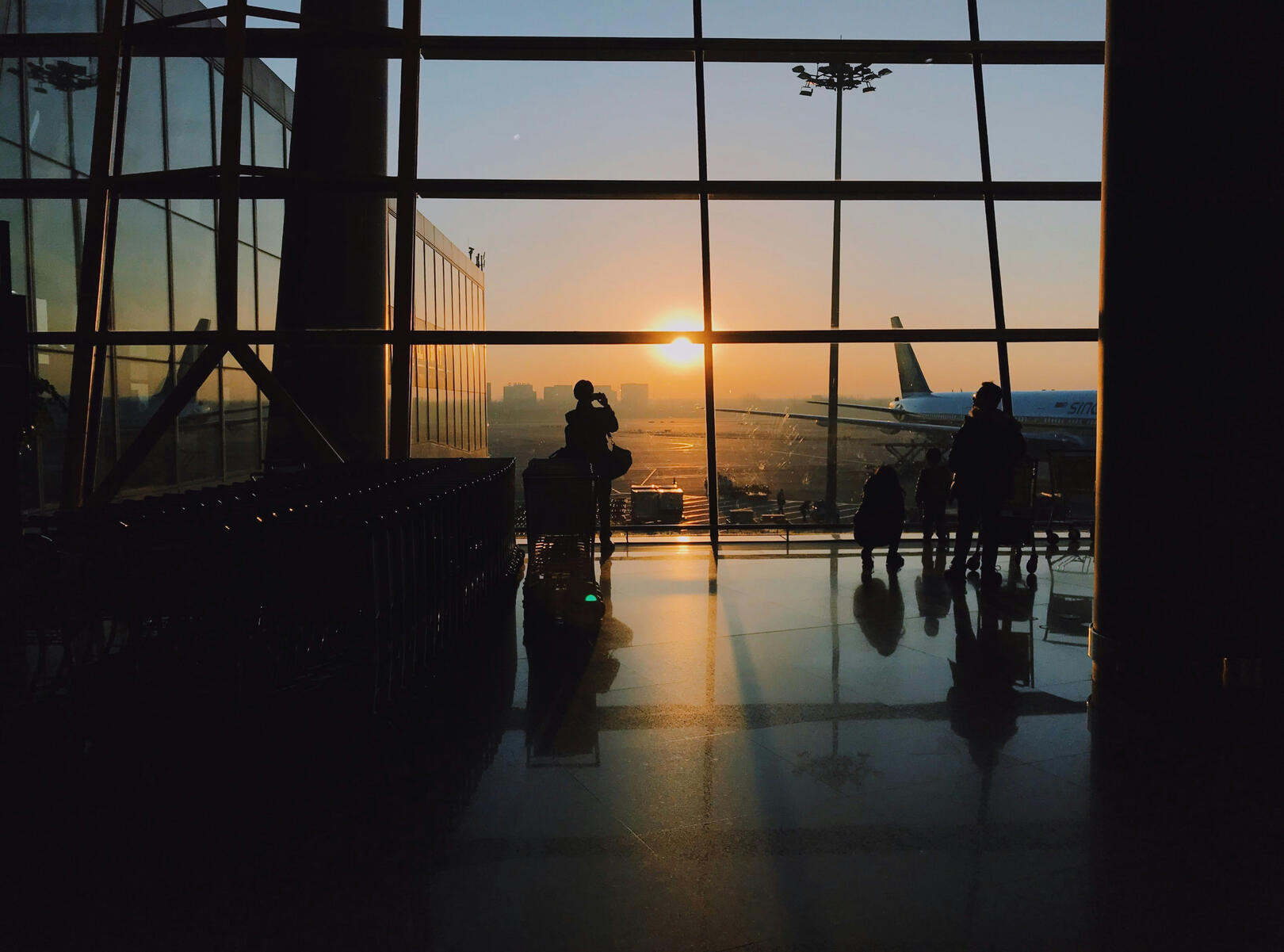 airport terminal Sunset view from airport terminal window, silhouetted passengers watching planes and city skyline